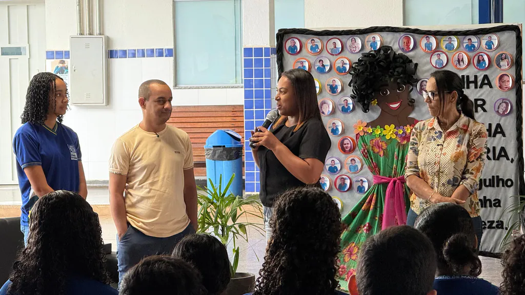 Pelézinho, de camiseta clara, ao lado de uma aluna e de duas mulheres, uma delas falando ao microfone, durante a roda de conversa na Escola Dr. Anísio José Moreira