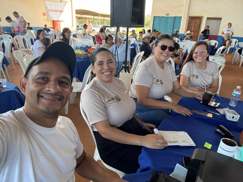 Pelézinho, de boné, faz uma selfie com três integrantes da equipe na mesa da organização do leilão da APAE, com o público sentado às mesas ao fundo