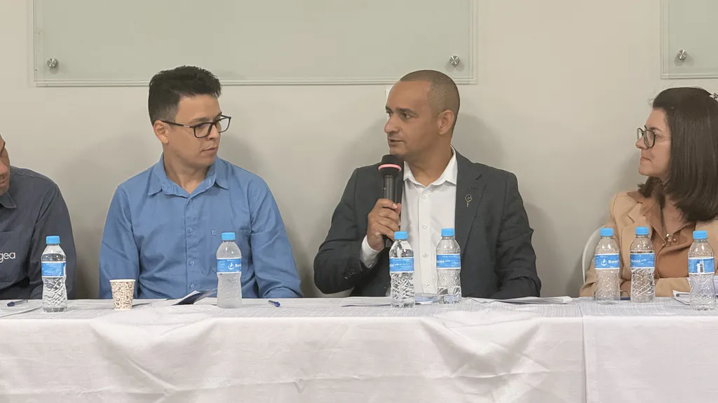 Pelézinho, de terno escuro, fala ao microfone na mesa da audiência pública sobre o abastecimento de água em São José do Rio Claro